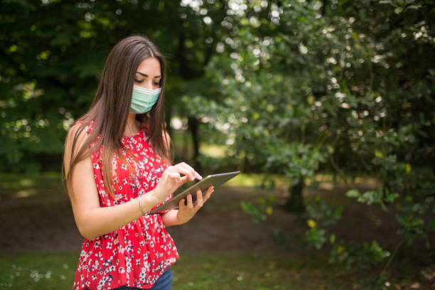 istock Young woman wearing protective mask using digital tablet in park 2182894245