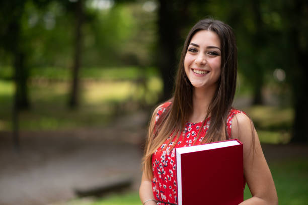 istock Smiling student holding a book in a park: education concept 2182895469