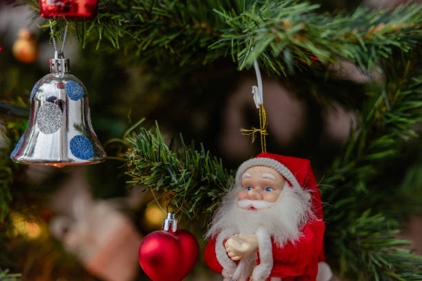 Close-up of a Santa Claus decoration with a decorated Christmas tree in the background.