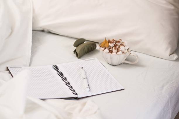 Woman writing in journal in bed, relaxing and thinking about personal wellbeing.