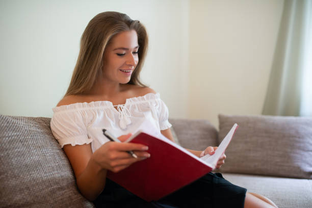 istock Young woman reading notes on sofa at home 2182902700