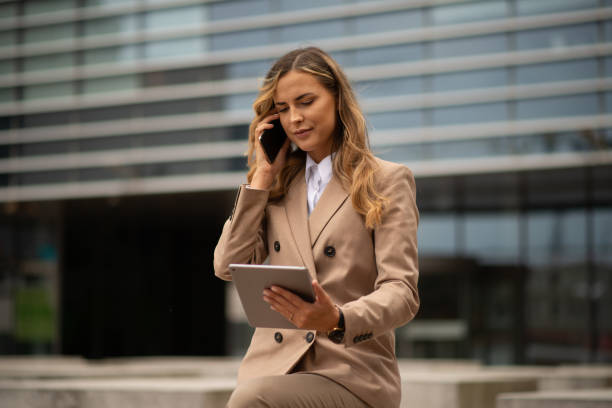 istock Businesswoman multitasking with phone and tablet outside office 2182903712