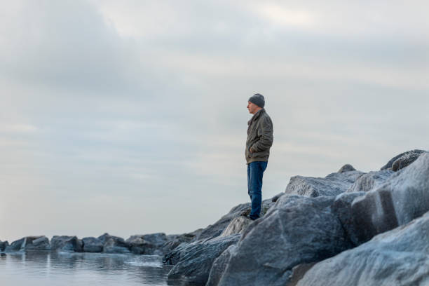 Man standing alone on rocks looking out to sea, cold weather