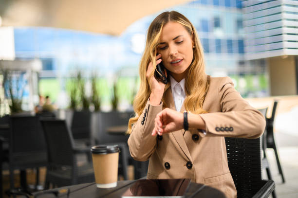 istock Businesswoman checking time while talking on phone at outdoor cafe 2182907147