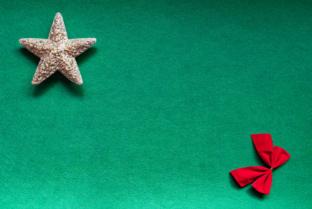 Golden Christmas star and red bow on green background isolated in composition leaving copy space in the center