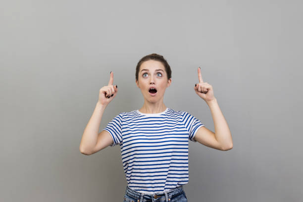 istock Woman pointing fingers up on empty space, amazed by advertisement area, keeps mouth opened. 2182926212