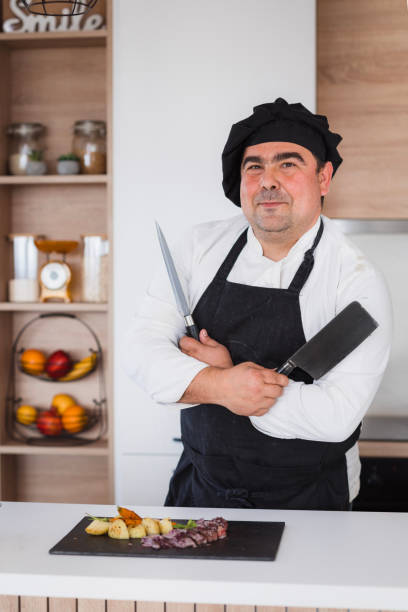 istock Chef standing by steak dish and holding a knife and cleaver 2182926536