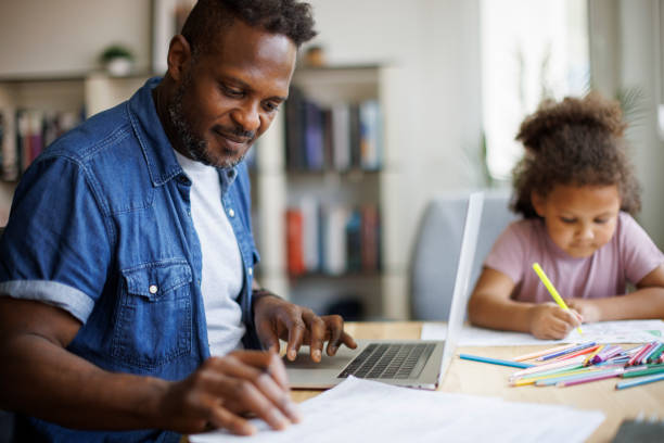 istock Father working on laptop while his daughter doing homework beside him at home 2182931912