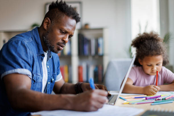 istock Father working on laptop while his daughter doing homework beside him at home 2182931923