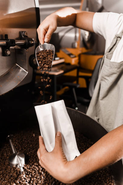 istock Packing roasted coffee beans into a craft bag. Pouring fried coffee grains in packaging bag in the facility. 2182932771