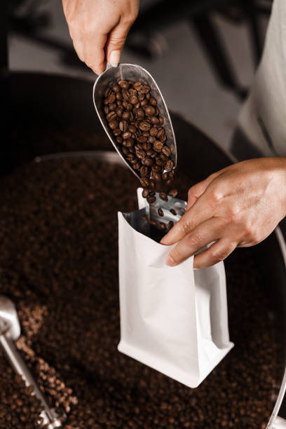 istock Filling coffee grains in a craft bag. Packing fried coffee beans. Worker pouring roasted coffee beans in packaging bag. 2182932784