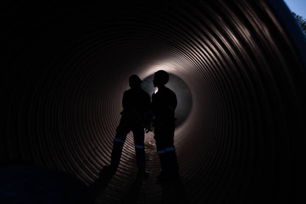 istock Two male construction engineers, with flashlights and safety equipment, inspect the availability of large drainage pipe materials before commissioning the underground system. 2182935996