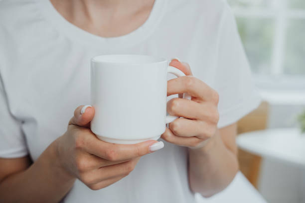 istock A person holding a plain white mug while sitting in a bright, cozy room during the morning 2182944098