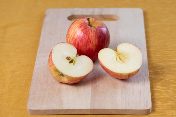 Whole apple and apple cut into two parts on a wooden board, yellow background