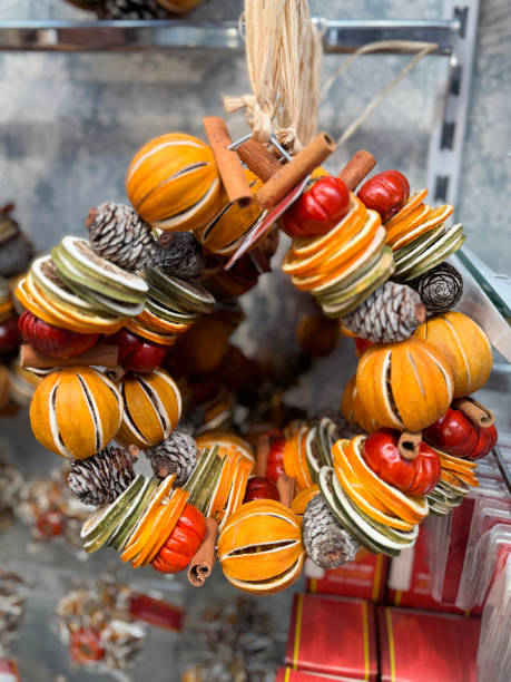 istock Full frame image of Christmas decorations, wreaths of wire frame strung with whole split and sliced dried citrus fruits (oranges and limes), pine cones, mini pumpkins and cinnamon sticks, hanging by raffia loop on retail display, focus on foreground 2182950650