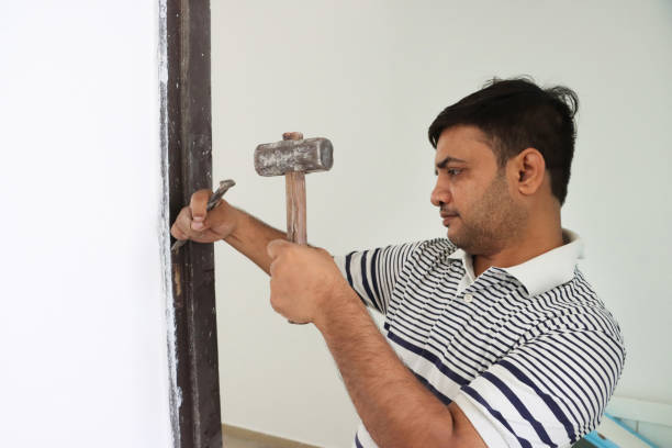 istock Image of skilled handyman using hammer and chisel on stuck door hinges, adjusting flathead screws and frame 2182951063