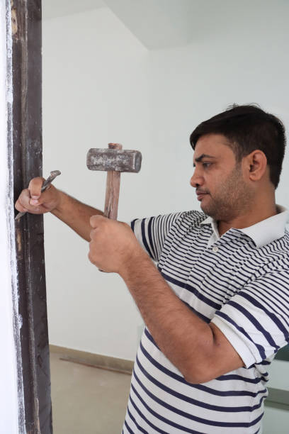 istock Image of carpenter fixing stuck door hinges with hammer and chisel, adjusting flathead screw, refining door frame 2182951064