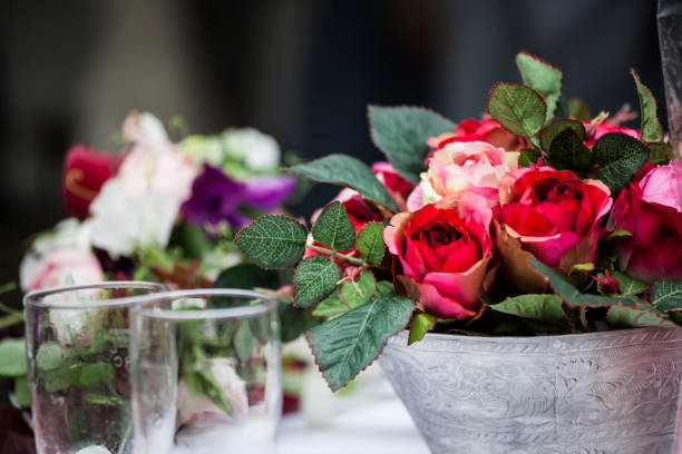 A beautiful arrangement of roses in rich colors sits elegantly alongside glasses, enhancing the festive atmosphere at a wedding celebration. The vibrant florals create a stunning centerpiece.