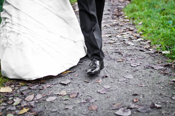 The bridal pair strolls hand in hand on a charming path, surrounded by fallen leaves, capturing a moment of joy during their wedding day in a serene outdoor location.