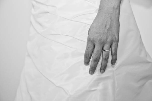 A close-up of a bride's hand resting gently on her satin wedding gown, showcasing an elegant engagement ring. The soft fabric complements the precious moment of celebration and love.