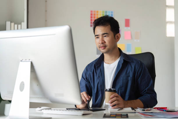 istock Young Male Graphic Designer Focused on Creative Work at Computer in Modern Office Environment 2182976235