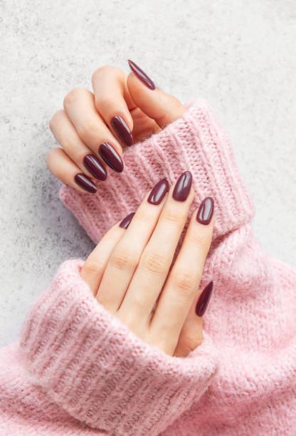 istock Elegant maroon manicured nails displayed against a soft pink sweater on a textured gray background 2182990023