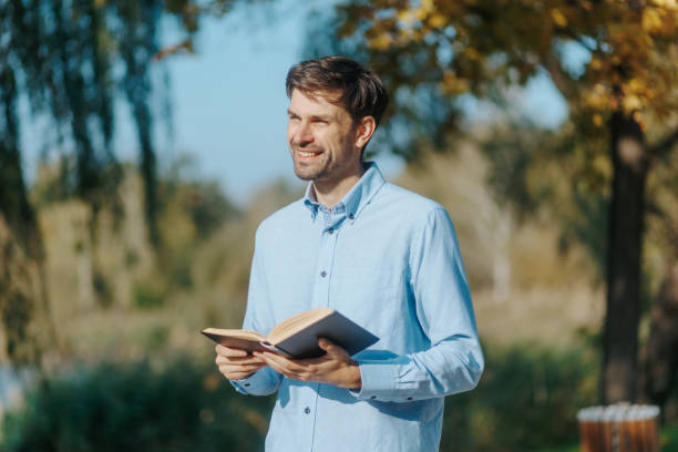 istock Man Absorbed in Book During Peaceful Walk Through Scenic Park 2182990201