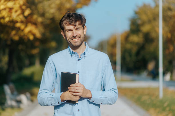 istock American Man Takes a Relaxed Park Walk, Engrossed in a Book 2182990215