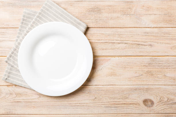 istock Top view on colored background empty round white plate on tablecloth for food. Empty dish on napkin with space for your design 2182997044