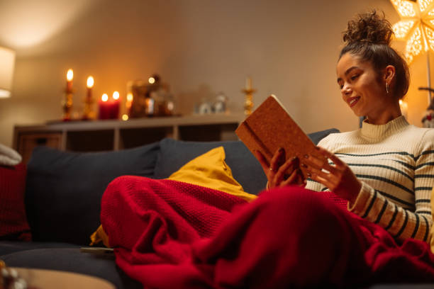 istock Young woman reading a book on sofa at home during christmas time 2182998995