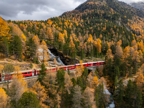 istock Red Train Passing Through Golden Autumn Forest and Waterfall 2183000073