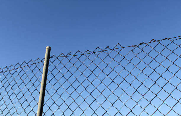 istock Section of old chain-link fence against a bright blue sky 2183009757