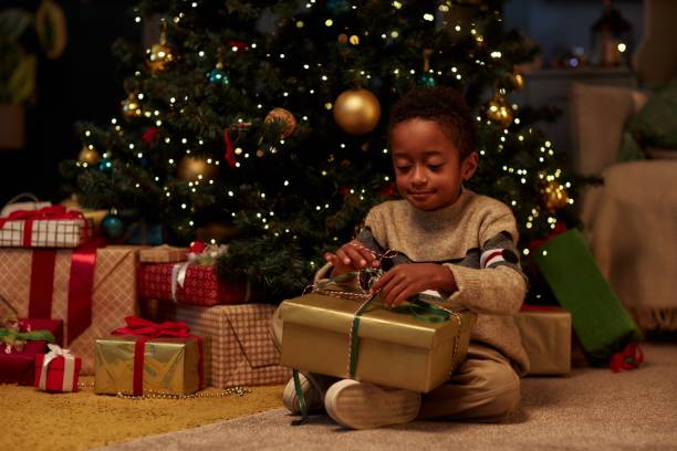 istock Smiling Black Child Holding Big Gift Box by Christmas Tree 2183012834