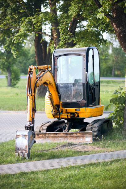 istock Tracked orange mini excavator digger near road green with trees on background with copyspace vertical shot. 2183014166