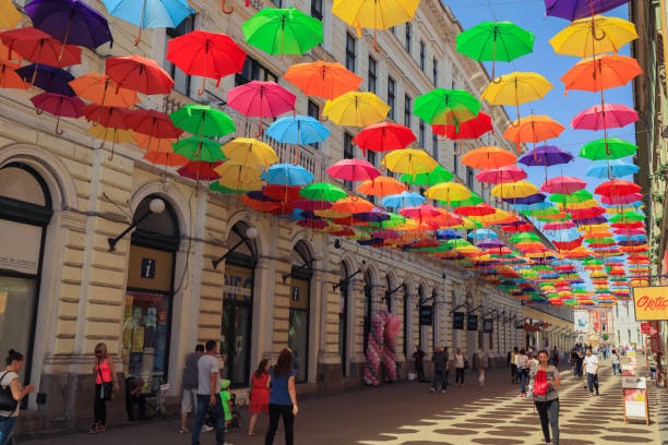 Timisoara, Romania - May 23, 2023: A lively street in Timisoara is adorned with an array of colorful umbrellas hanging overhead creating a cheerful and inviting atmosphere for pedestrians enjoying a sunny summer day.