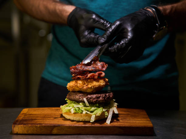 A man is preparing a burger with bacon and lettuce