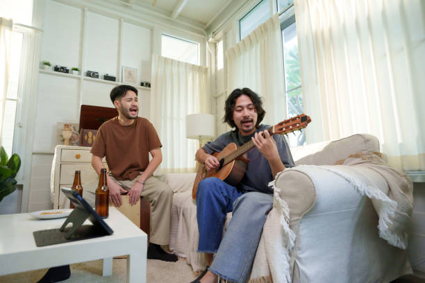 istock Asian man playing guitar while his friend plays a cajon, both singing and enjoying a musical jam session in a living room. Friendship concept. 2183027577