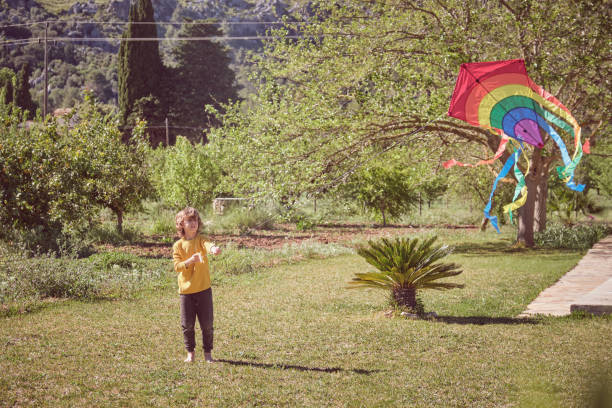 Small boy twisting kite while wind died down on journey on rocky hillside