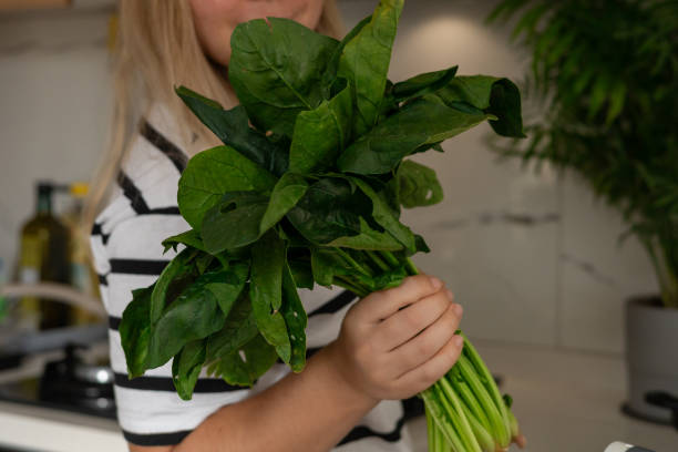 istock Young woman holding fresh spinach in a modern kitchen while preparing a healthy meal 2183037223