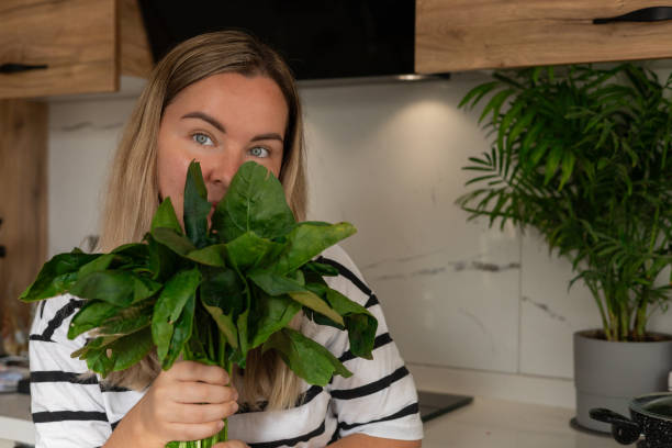 istock Woman happily holding fresh spinach in a modern kitchen during daylight 2183039037