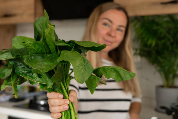 istock Young woman holding fresh spinach in a modern kitchen while preparing a healthy meal 2183039547