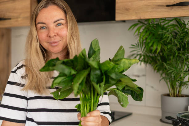 istock Young woman holding fresh spinach in a modern kitchen while preparing a healthy meal 2183039905