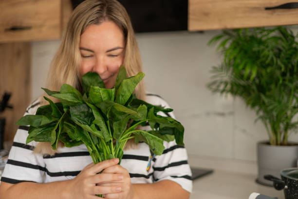 Woman happily holding fresh spinach in a modern kitchen during daylight