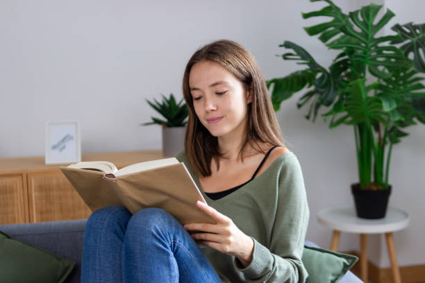 istock Young woman reading a book at home on the sofa 2183042734