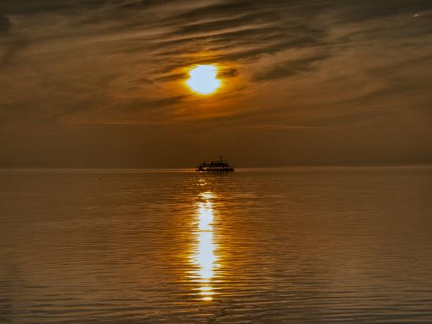 A serene sunset over calm waters with a silhouette of a boat on the horizon, casting a golden reflection.