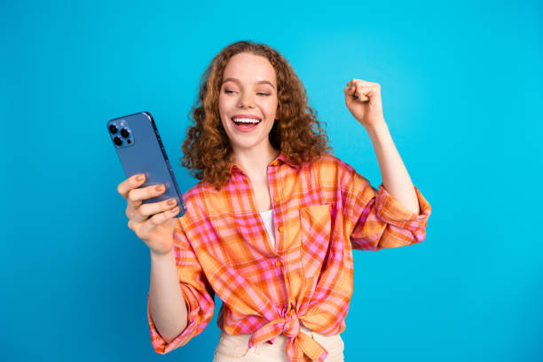 istock Joyful young woman celebrating success while checking her phone over vibrant blue background 2183046531