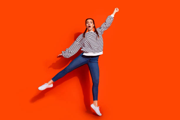 istock Young woman in casual striped pullover striking a vibrant pose against a bold orange background 2183053098