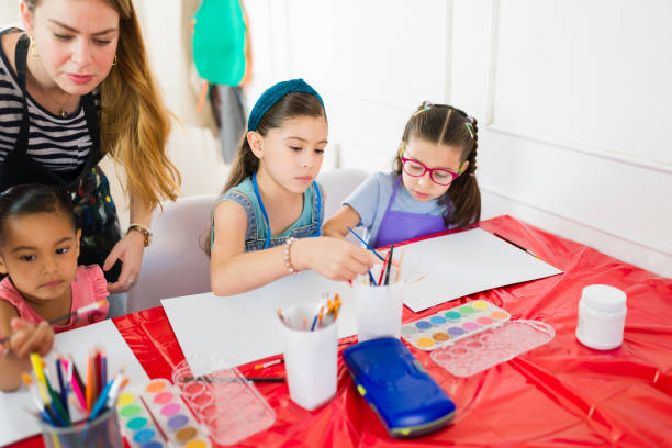 istock Teacher assisting elementary school students in painting with watercolors during art class 2183053784
