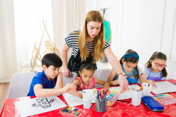 istock Caucasian art teacher helping diverse elementary school students painting with watercolors during art class 2183054165