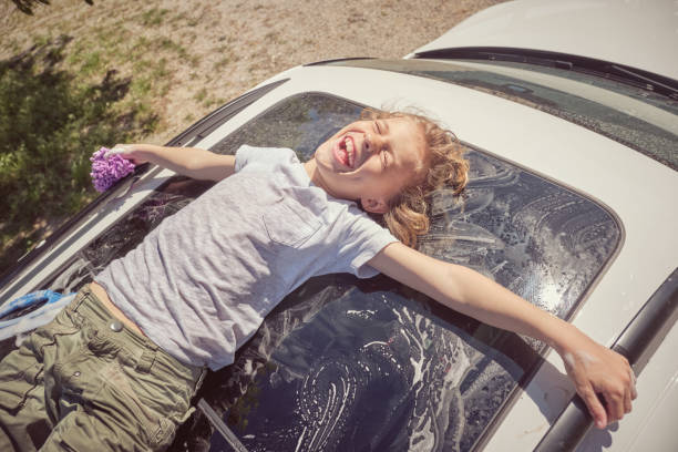 A man is thoroughly cleaning his car in an outdoor area using a sponge soaked with suds, ensuring it sparkles for better maintenance and appearance.